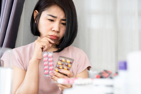 Asian woman thinking and doubt of taking antibiotics and anti-inflammatory drugs togetherの写真素材