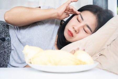 Asian woman's post-Durian overindulgence experiencing headache and dizziness due to excessive consumptionの写真素材