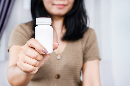 Asian woman holding a blank white squeeze bottle plastic tube for pills, capsules, or supplements. mockup packaging concept.の写真素材