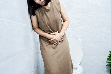 Asian woman tired from chronic diarrhea resting against the wall in the toilet hand holding stomachacheの写真素材