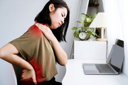 Asian Woman suffering Neck, Shoulder, and Lower Back Pain due to Office Syndrome from Prolonged Computer Workの写真素材