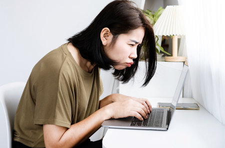 Asian Woman having problems with Blurry Vision and Eye Strain while Working on a laptop sitting too close to the screen, Computer vision syndrome or  digital eyestrain symptoms conceptの写真素材