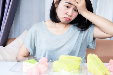 sad Asian woman feeling guilty after eating too many sweets dessertsの写真素材