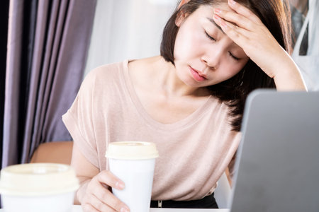Asian woman suffering from headaches after drinking too much coffee, caffeine side effects concept