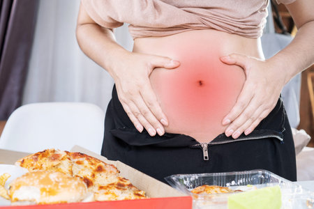 woman holding stomachache after over eating junk food pizza have problem with digestive systems