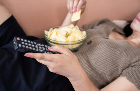 eating disorder ,unhealthy eating salty snack with woman lay down with potato chips and remote tv in handsの写真素材