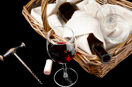 The glass of wine and picnic basket with bottle of wine on a blackの写真素材