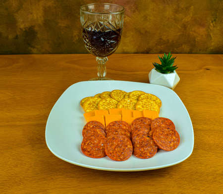 a snack plate consisting of crackers, cheeseand pepperoni with a glass of wineの写真素材