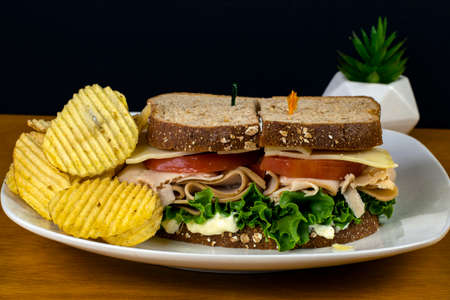 chicken sandwich  with swiss cheese and tomato and a side of potato chipsの写真素材