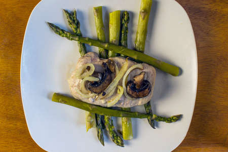 porkl chop with sauteed onions and mushroom resting on asparagusの写真素材