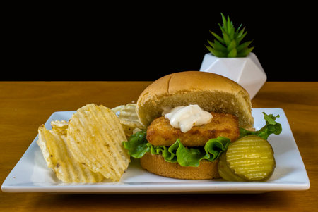 a fish sandwich  with onions and lettuceand potato chipsの写真素材