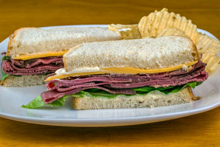 roast beef sandwich top with cheese and mayonnaise and served with potato chipsの写真素材