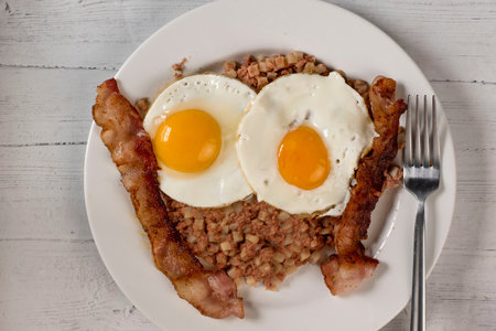 two fried eggs on corn beef hash  served with baconの写真素材