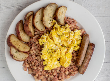 scramble eggs on corn beef hash  served with breakfast links and potato wedgesの写真素材