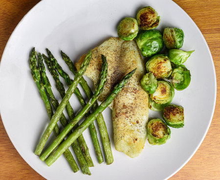 baked seasoned tilapia  served with roasted brussel sprouts and asparagus,の写真素材