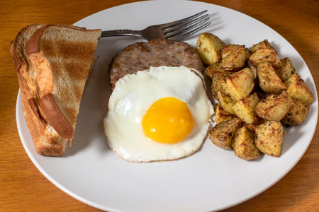 fried egg  on sausage patty served with  home fries and toastの写真素材