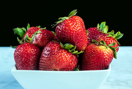 strawberries arranged in a bowl against a black back groundの写真素材