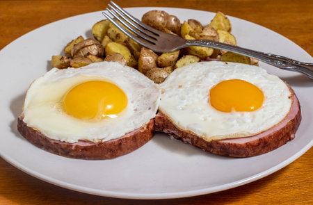 fried eggs on ham  served with home friesの写真素材