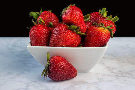 strawberries arranged in a bowl against a black back groundの写真素材