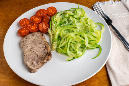 baked pork chop served with  zucchini noodles and tomatoesの写真素材