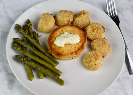 salmon burger top with tarter sauce served with baked scallops and asparagus
