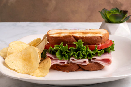 ham with lettuce and tomatoes on toasted white bread served with chipsの写真素材