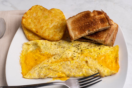 cheese onelette  top with  seasoning served with  hash browns and toastの写真素材