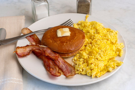 scramble eggs  with bacon  served with pancakes top with  syrup andbutter