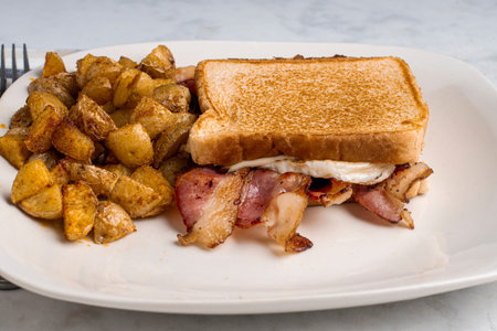 fried egg and bacon cheese melt sandwich served with home fries.