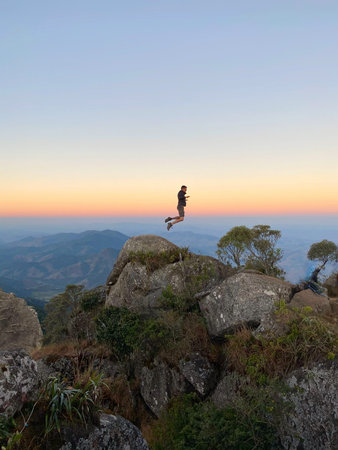 Man jumping over the rocks at sunset in the mountains, on the peak of the sealed rock.