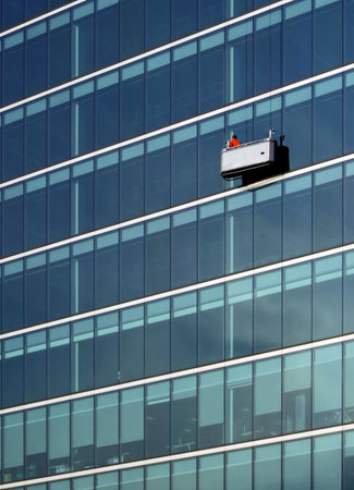 A solitary red anonymous cleaner of a perspective corrected modern office block.  Note: there is some very fine near invisible grain at 100%.の写真素材