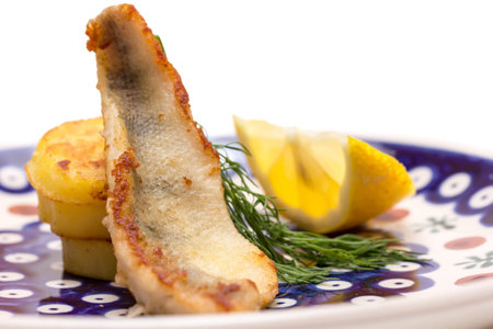 Perch filet with fried potatoes, lemon and dill in a blue plate
