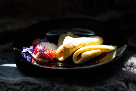 Pancakes with cut strawberries and cream on black plateの写真素材
