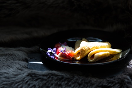 Pancakes with cut strawberries and cream on black plateの写真素材