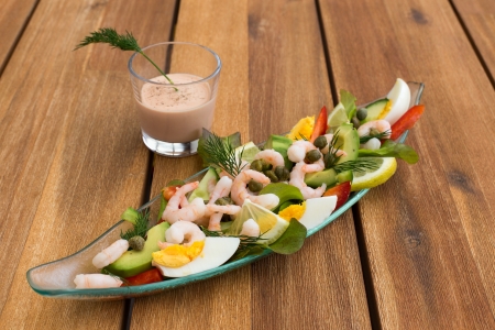 Shrimp cocktail with avocado, eggs, lemon and glass of sauce on a wooden table の写真素材