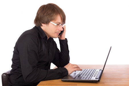 Young business man with black shirt and mobile phone working seriously on a laptop. Isolated on white background.の写真素材