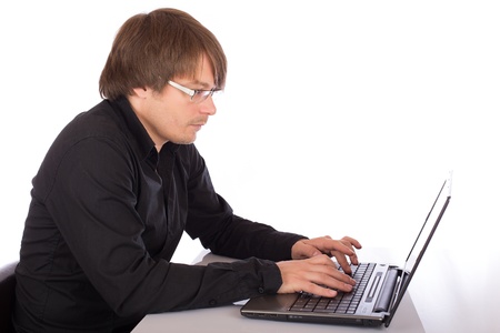 Concentrated young man with black shirt working seriously on a laptop. Isolated on white background.の写真素材