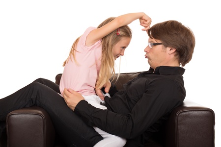 Young father play and make grimace to his daughter and she pointing her finger on his forehead in a brown leather armchair. Isolated on white background.の写真素材