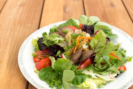 Salad with fried rabbit liver and fresh vegetables on a wooden table.の写真素材