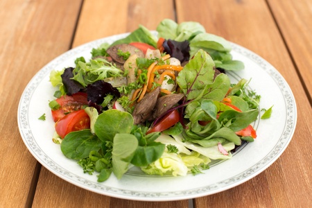 Mixed salad with fried rabbit liver and fresh vegetables on a wooden table.の写真素材