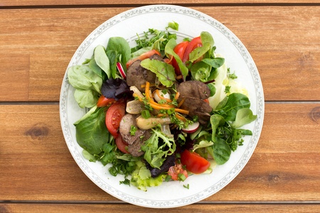 Summer salad with fried rabbit liver and fresh vegetables on a wooden table.の写真素材