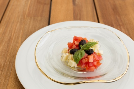 Fresh mozzarella and tomatoes tartar in glass plate on a wooden table.の写真素材