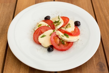 Delicious mozzarella, tomatoes salad in white plate on a wooden table.の写真素材