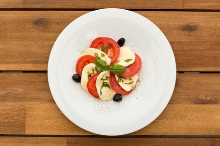 Tomatoes and mozzarella salad in white plate on a wooden table.の写真素材