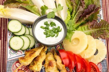 Asian food with chicken skewers, sauce, tomatoes, cucumber, pineapples, endives and salad.の写真素材