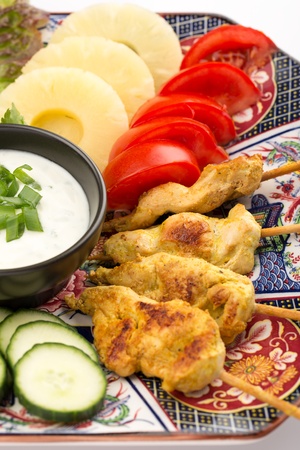 Asian food with chicken skewers, sauce, tomatoes, cucumber, pineapples, endives and salad.の写真素材