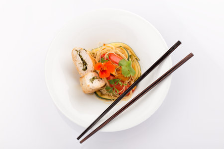 Asian food with piece of stuffed chicken, noodles, zucchini, carrots and tomatoes.