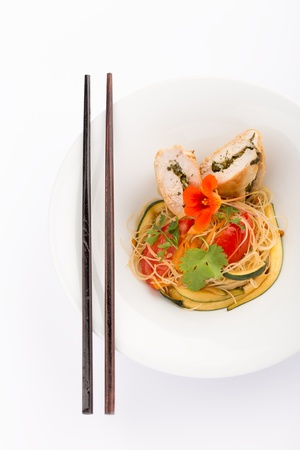 Asian food with piece of stuffed chicken, noodles, zucchini, carrots and tomatoes.の写真素材