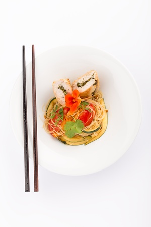 Asian food with piece of stuffed chicken, noodles, zucchini, carrots and tomatoes.の写真素材