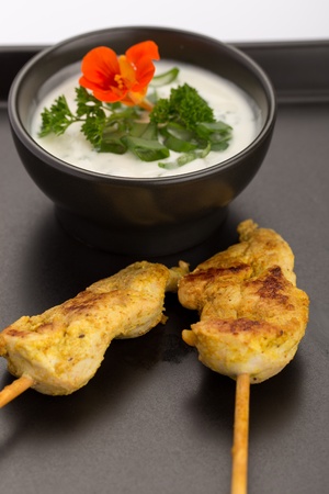 Chicken skewers and bowl of sauce on a black plate.の写真素材